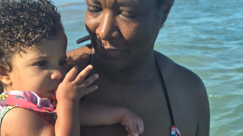 Black mom and biracial toddler daughter is sucking her thumb at the beach