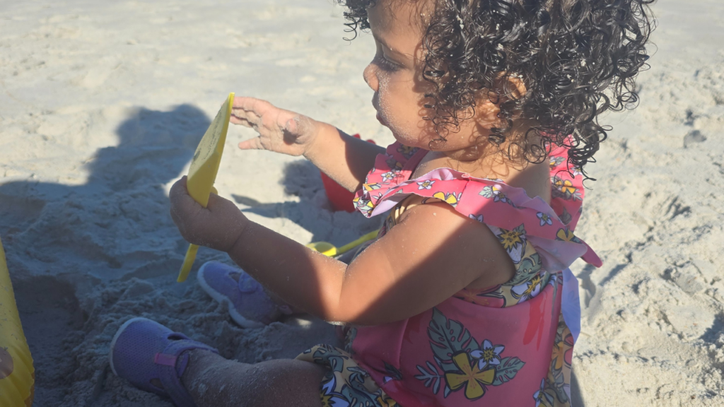 A biracial family of 4, parents putting reef safe sunscreen on their daughters, one toddler and one tween. The family is happy and excited to go to the beach