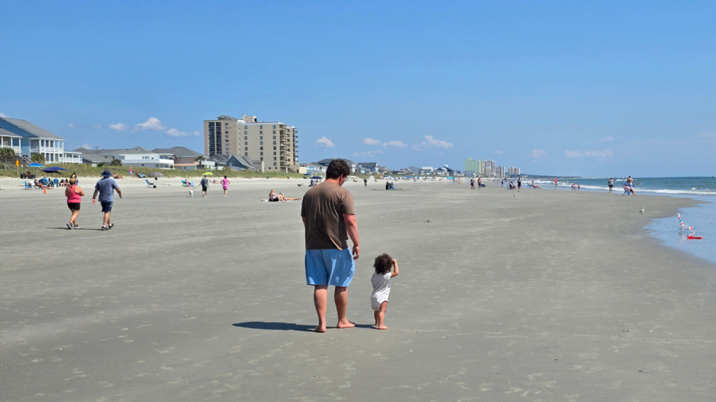 walking the shoreline observing patterns in the sand with toddler girl
