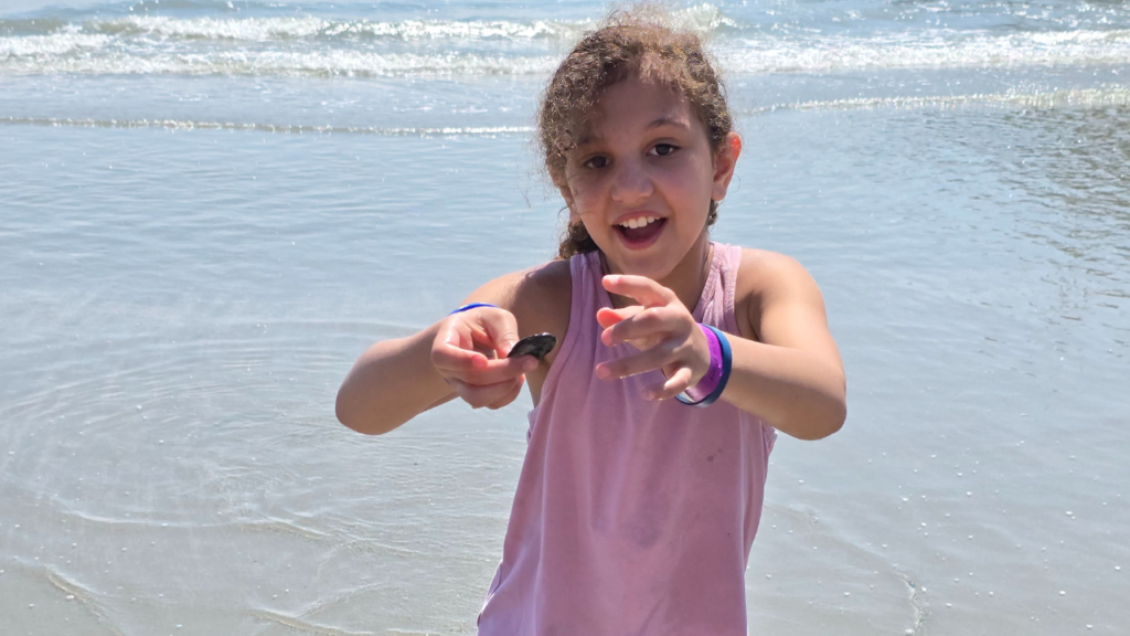 Spottinh shells on the beach but not taking any or putting them back where they were found. Girl is excitedly holding a shell she found on the beach.