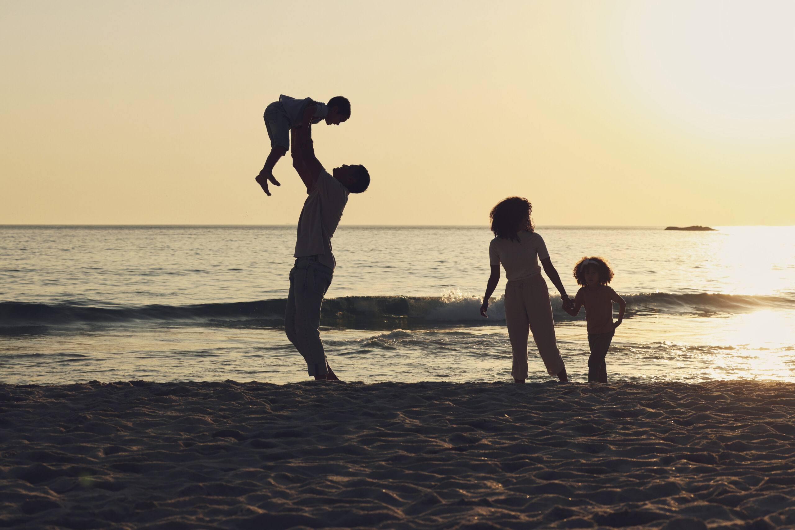Happy mixed race family with three children holding hands and walking along the beach and looking a.