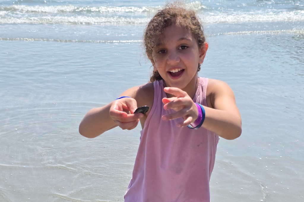 Spotting shells on the beach but not taking any or putting them back where they were found. Girl is excitedly holding a shell she found on the beach.