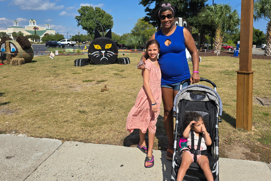 Black Mom and biracial tween daughter and biracial toddler daughter having fun, finding new places in the scavenger hunt. Daughter has peacy skirt and mom has on blue shirt and jeans. Baby is in stroller.